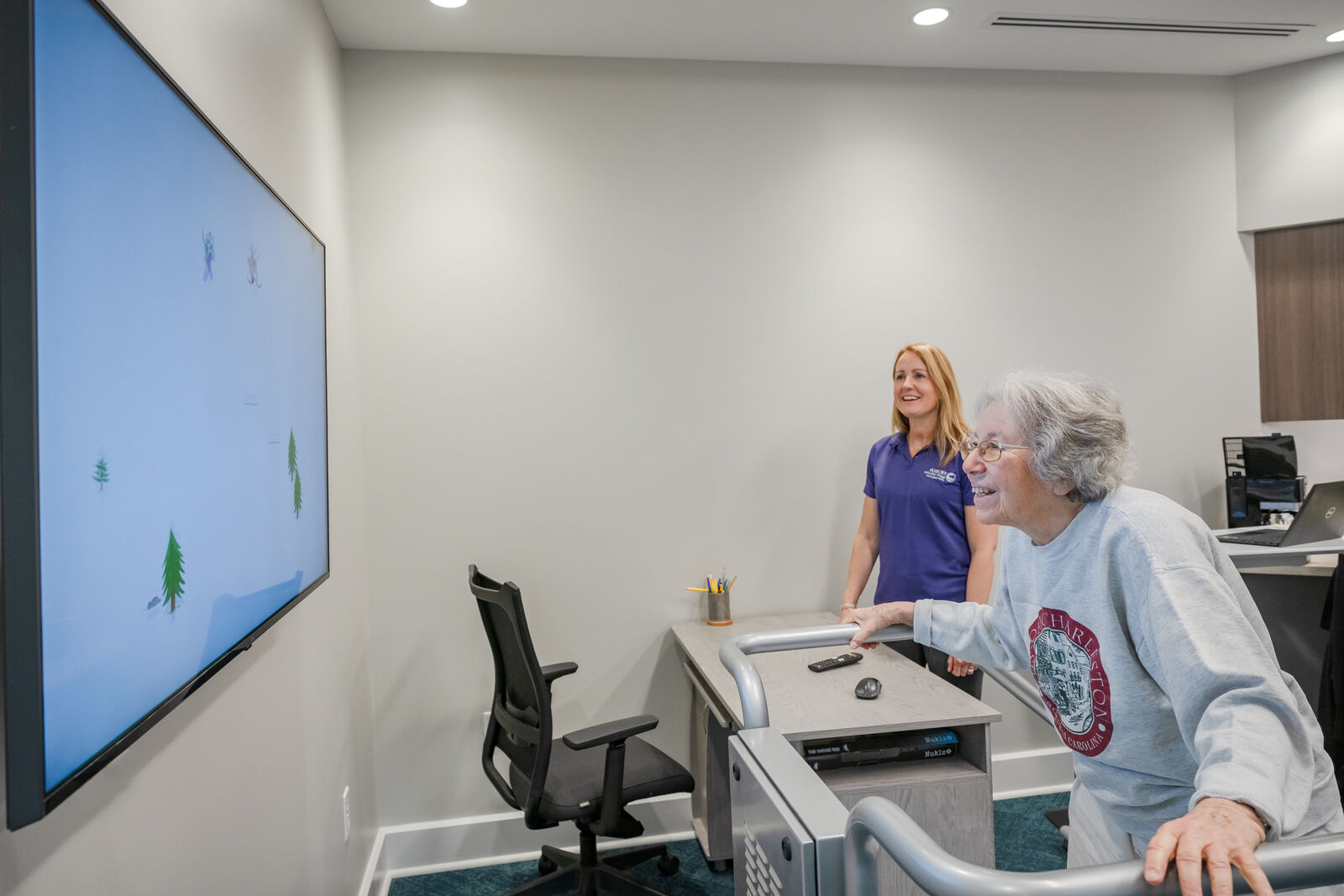 a woman using one of the brain health kinnections technology machines with brain health coach behind her