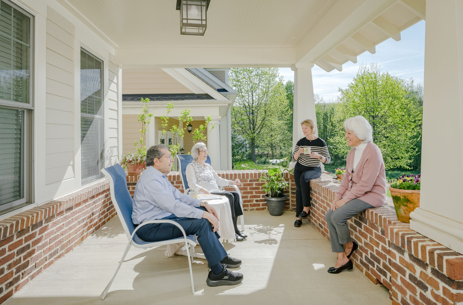 an older couple sitting on their porch, with a white woman and asian woman on their porch as well talking