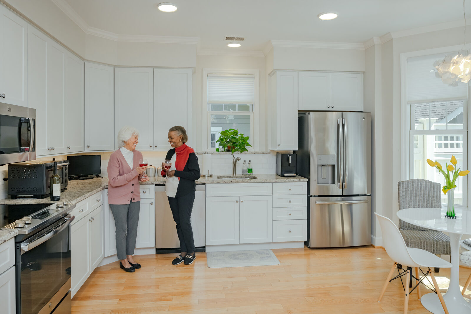 two older women enjoying wine in a bright white kitchen