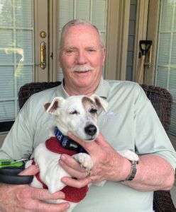 Springhill resident John Flynn, an older white man, with his dog in his lap on his outdoor patio. 