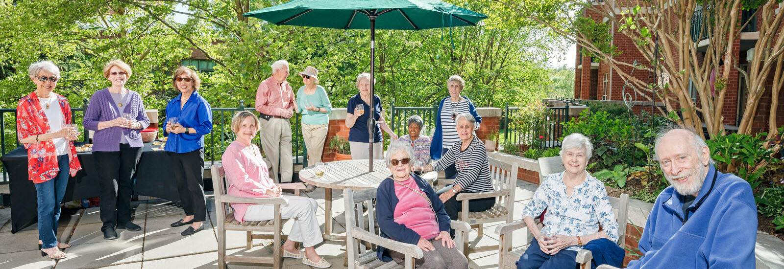 smiling group of seniors enjoy happy hour on large terrace outside Hefner Apartments