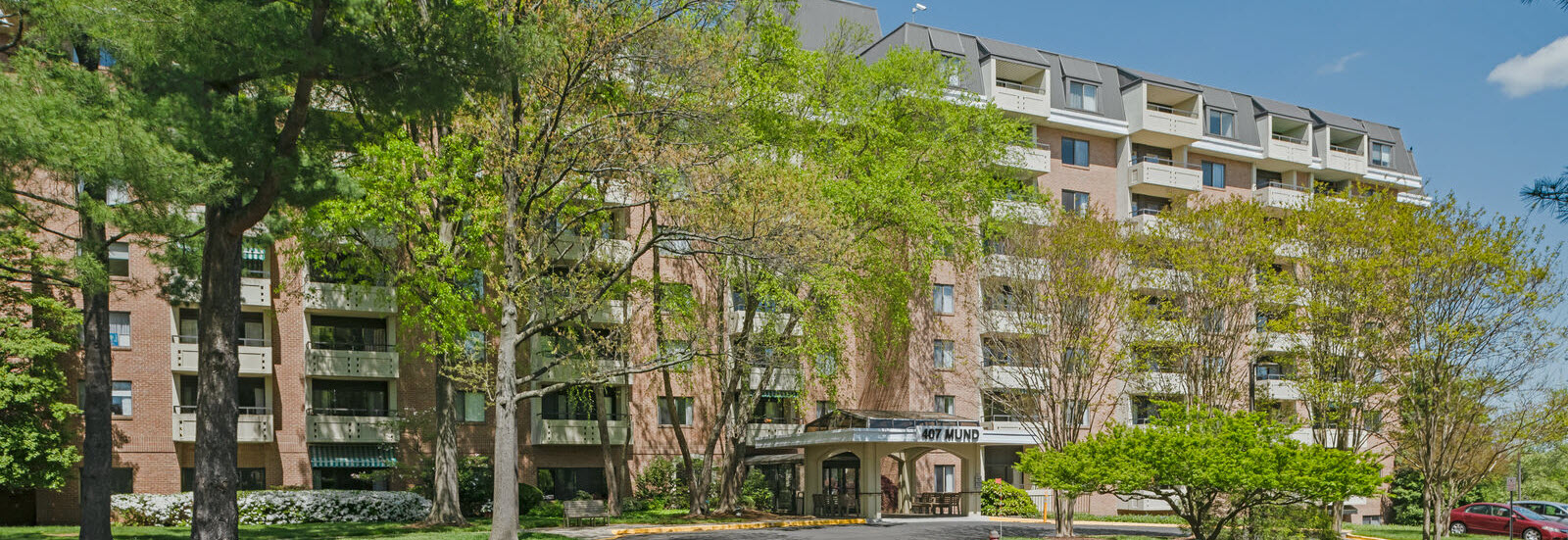 front exterior of Mund Apartments with green trees and covered entrance