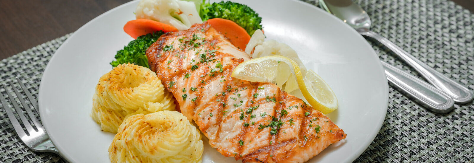 grilled salmon steak with lemon slice on a plate with mashed potato and steamed vegetables
